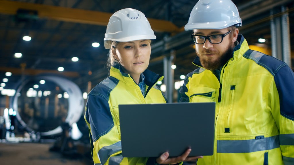 Ein Mann und eine Frau in Arbeitskleidung schauen auf ein Laptop als Nutzer von Factoring im Facility Management.