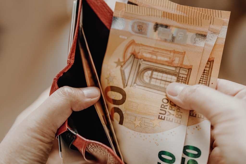 Blick auf drei 50 Euro-Scheine die eine Hand aus einem roten Portemonnaie nimmt zur Erfüllung des Zahlungsziels.