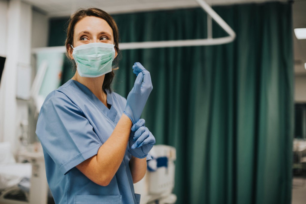 Eine Frau im Krankenhaus in Pflegekleidung zieht Einmalhandschuhe an. Nutzen Sie Factoring im Gesundheitswesen.