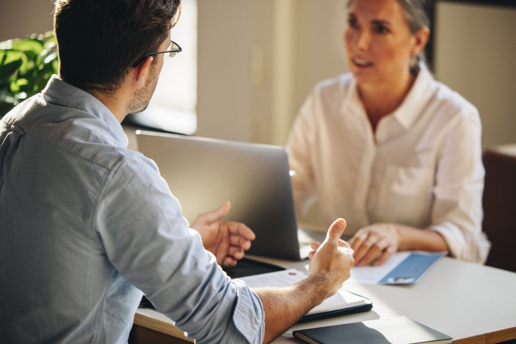 Ein Mann und eine Frau im Gespräch über Full Service Factoring sitzen einander gegenüber.